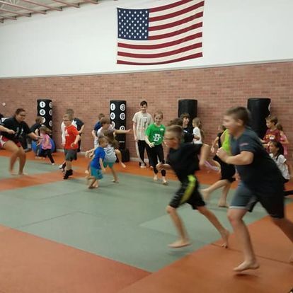 A group of children are running in a gym under an american flag