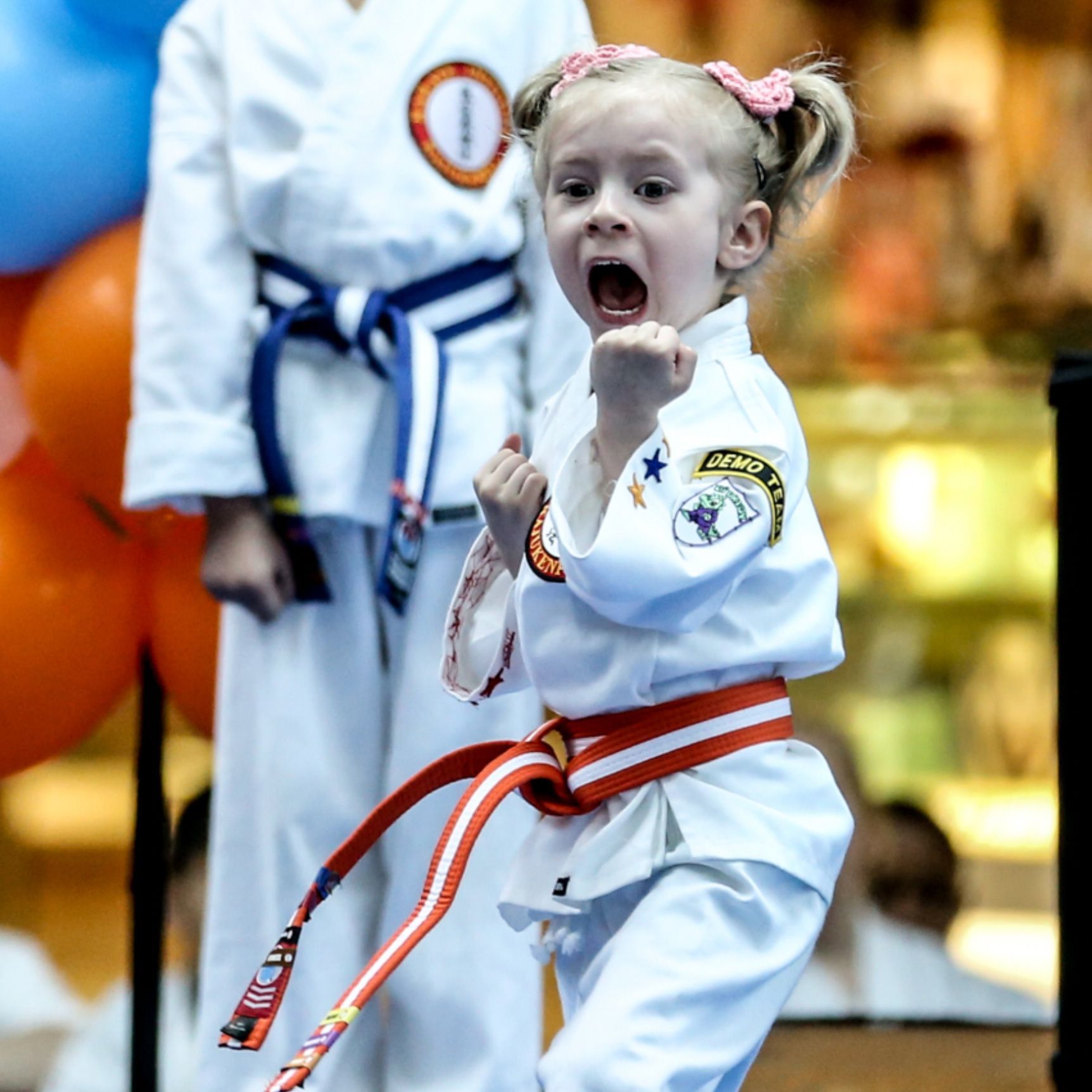 A little girl is wearing a white karate uniform and a red belt