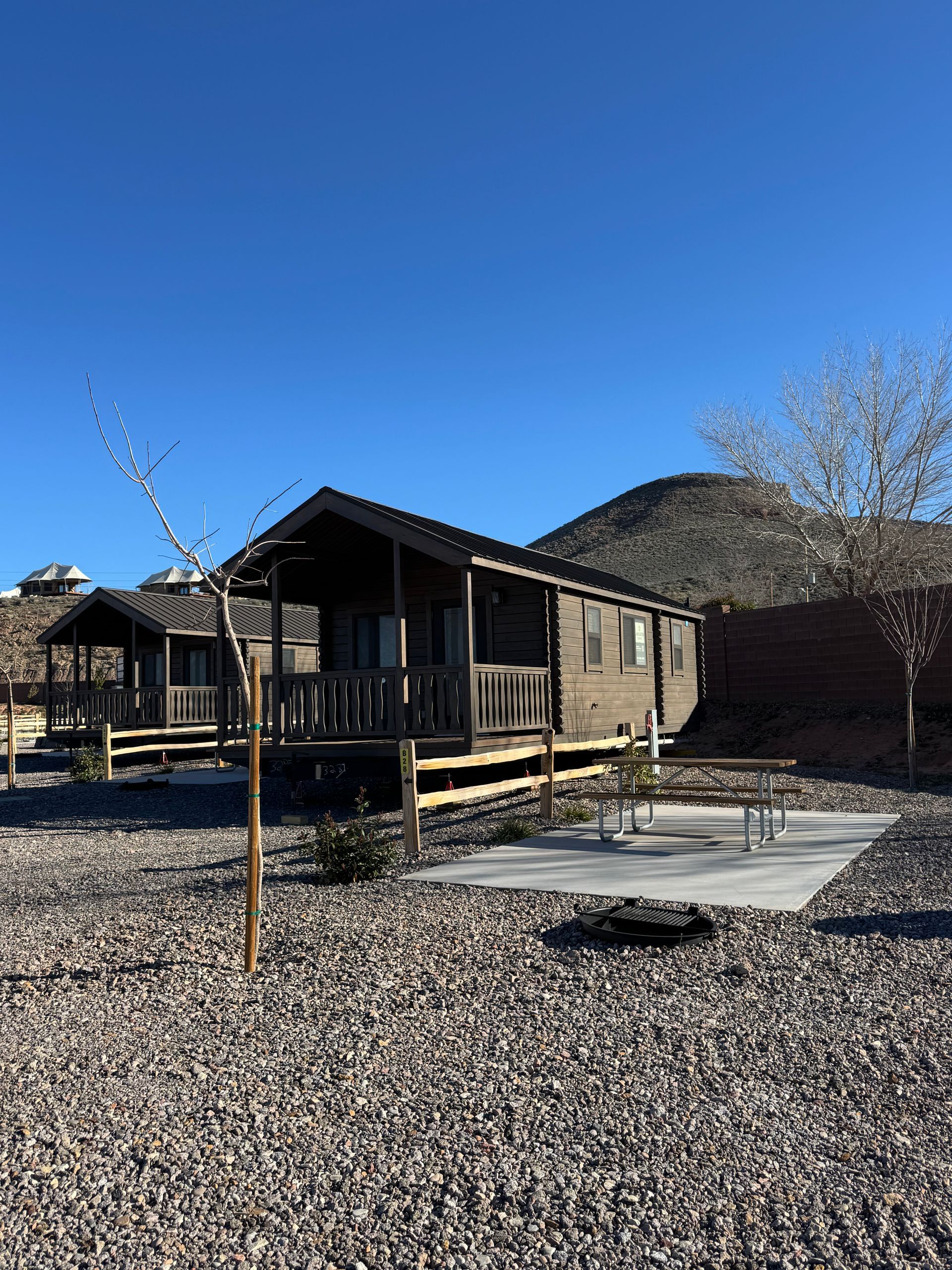Two small wooden rental cabins with porches and picnic tables set on a gravel lot under a clear blue sky.