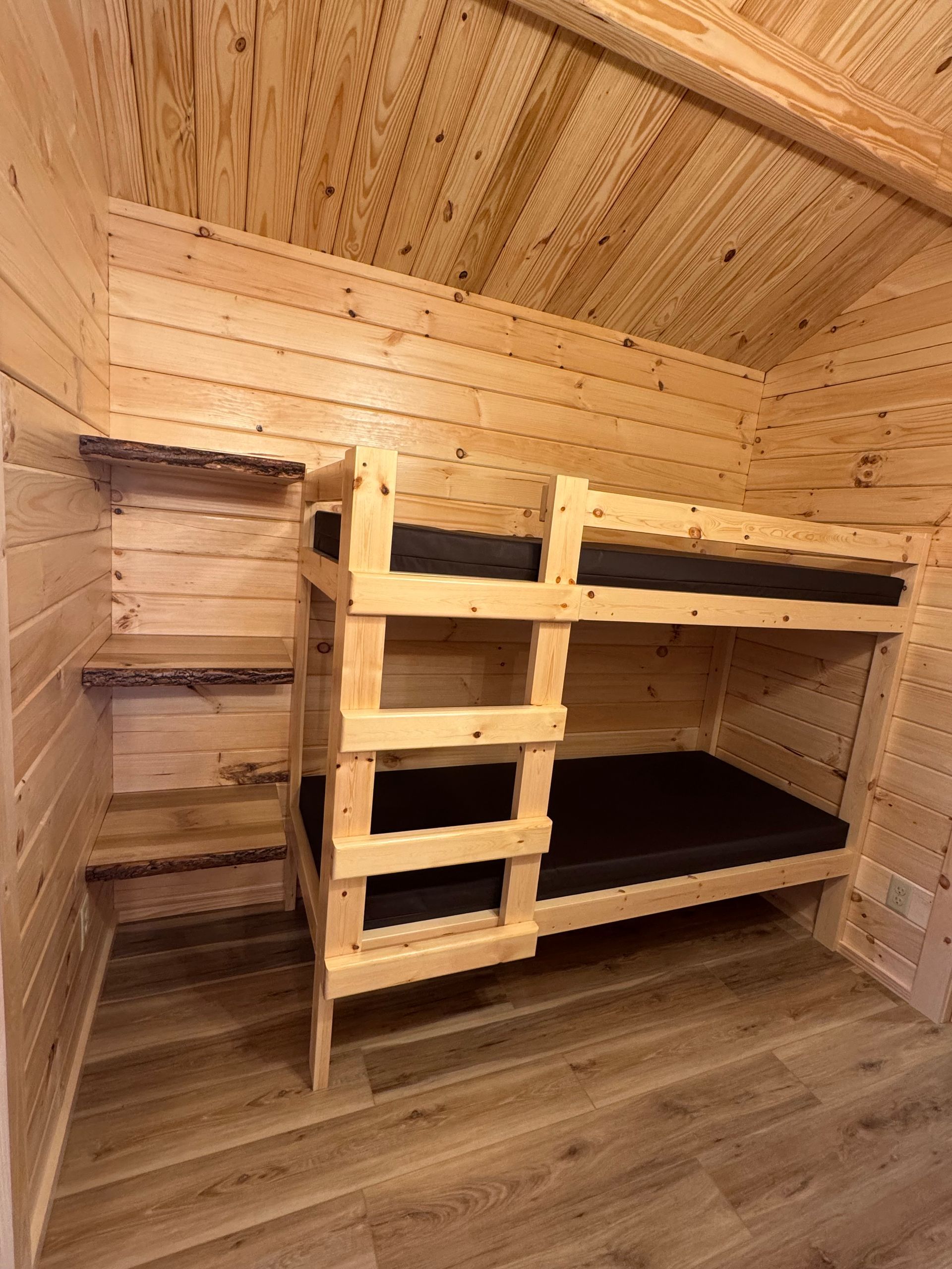 A bunk bed with black mattresses stands against a wood-paneled wall, next to built-in shelves with a natural wood edge.