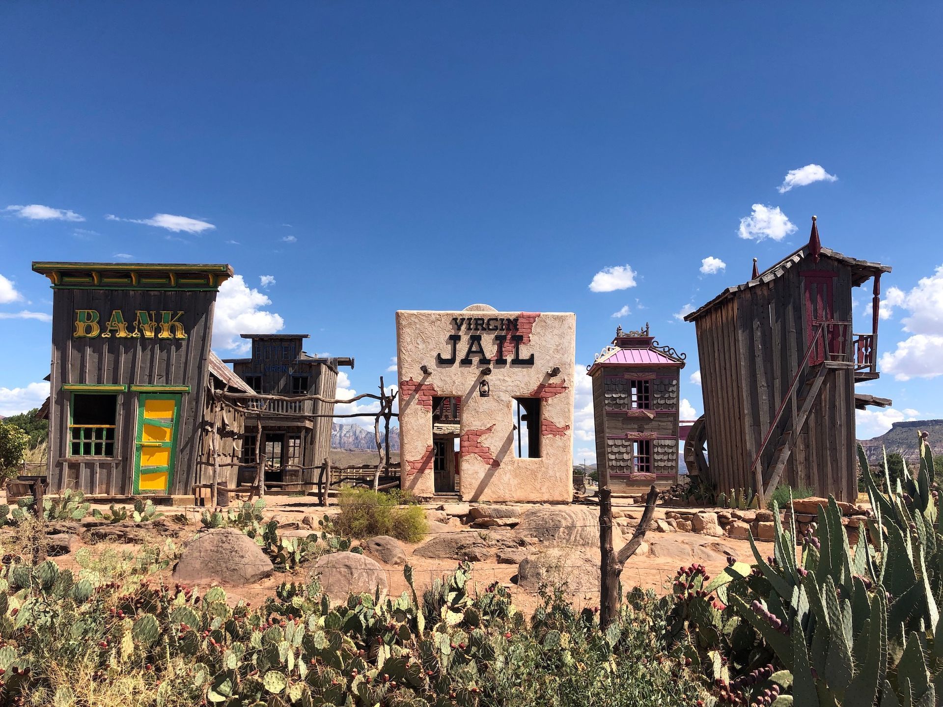 A western-style desert film set with a wooden bank, a tan jail, and weathered outbuildings surrounded by cacti.