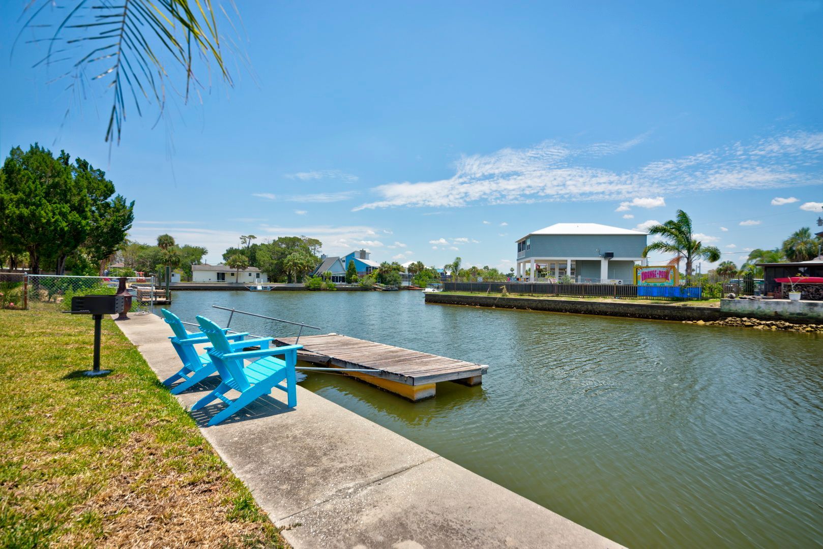 Two blue chairs are sitting on a dock next to a body of water.
