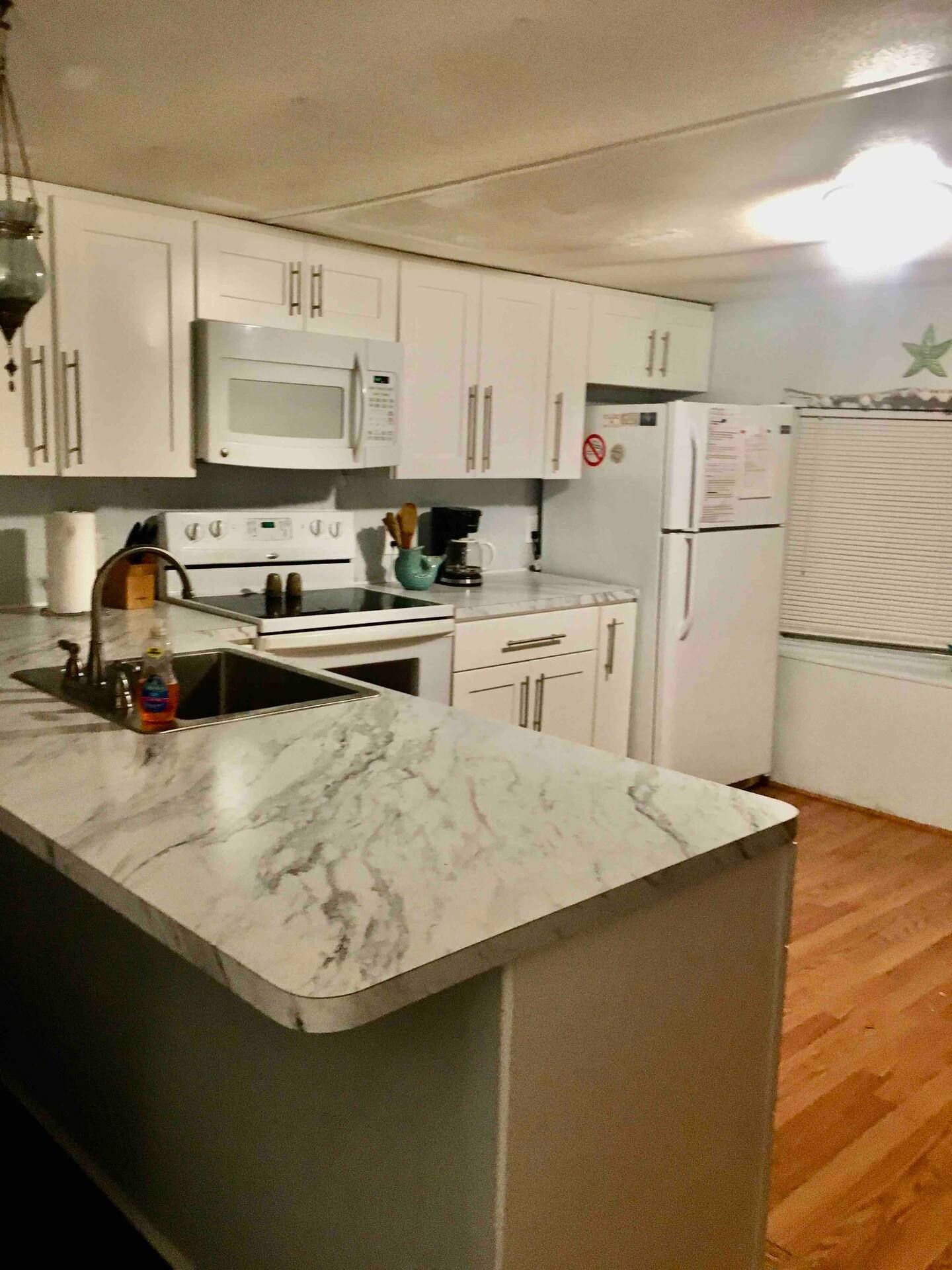 A kitchen with white cabinets , a refrigerator , stove , sink and microwave.