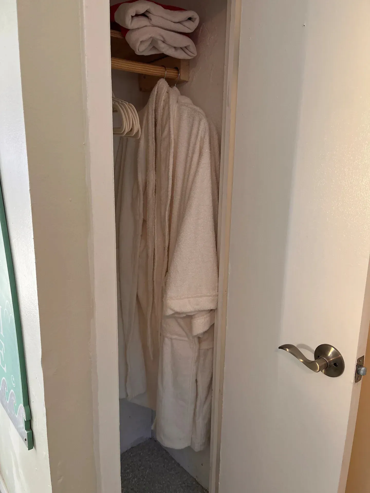 A white robe is hanging in a closet next to a door.