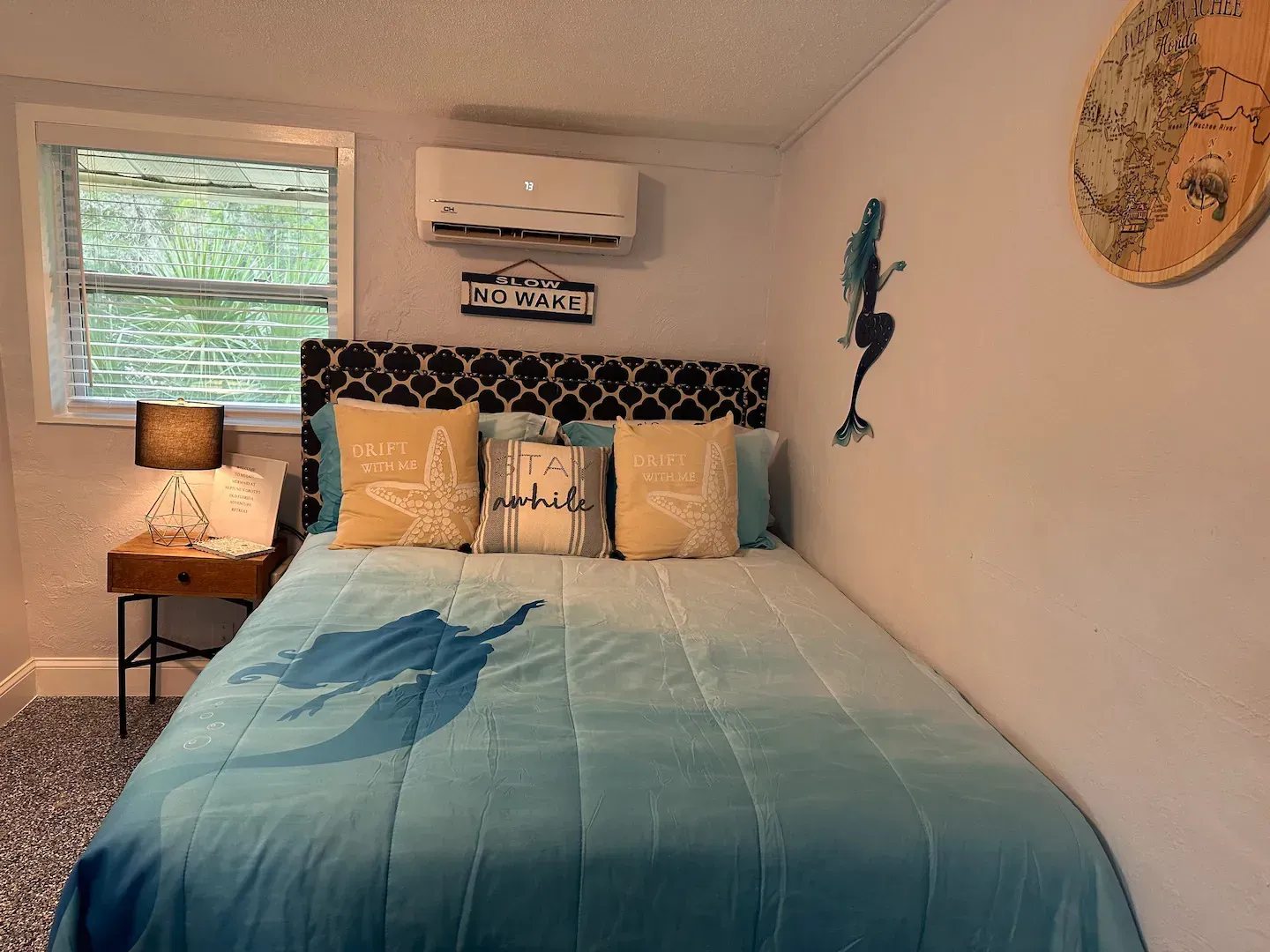 A bedroom with a bed , nightstand , lamp and window.