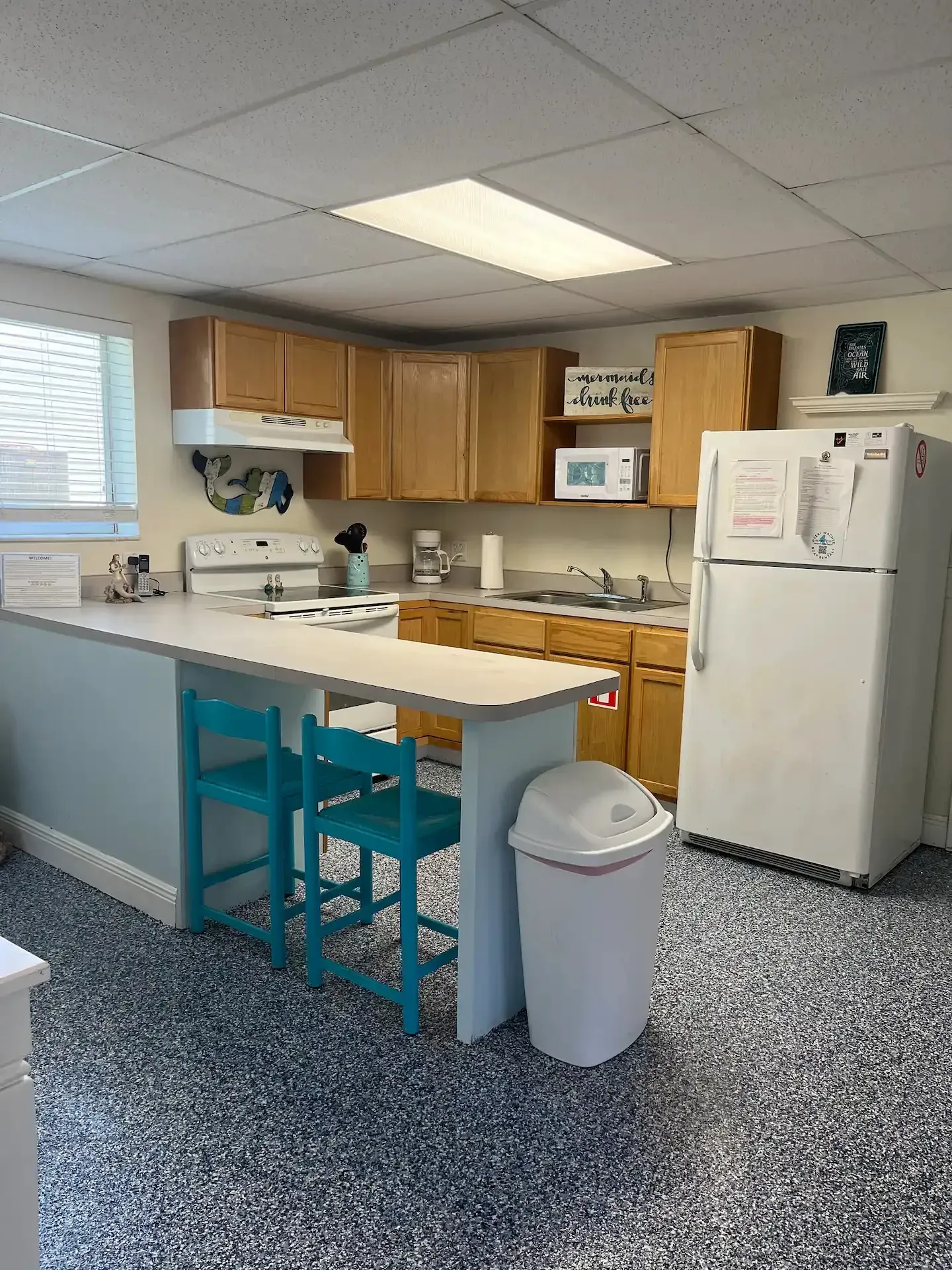 A kitchen with a refrigerator , stove , sink , and trash can.