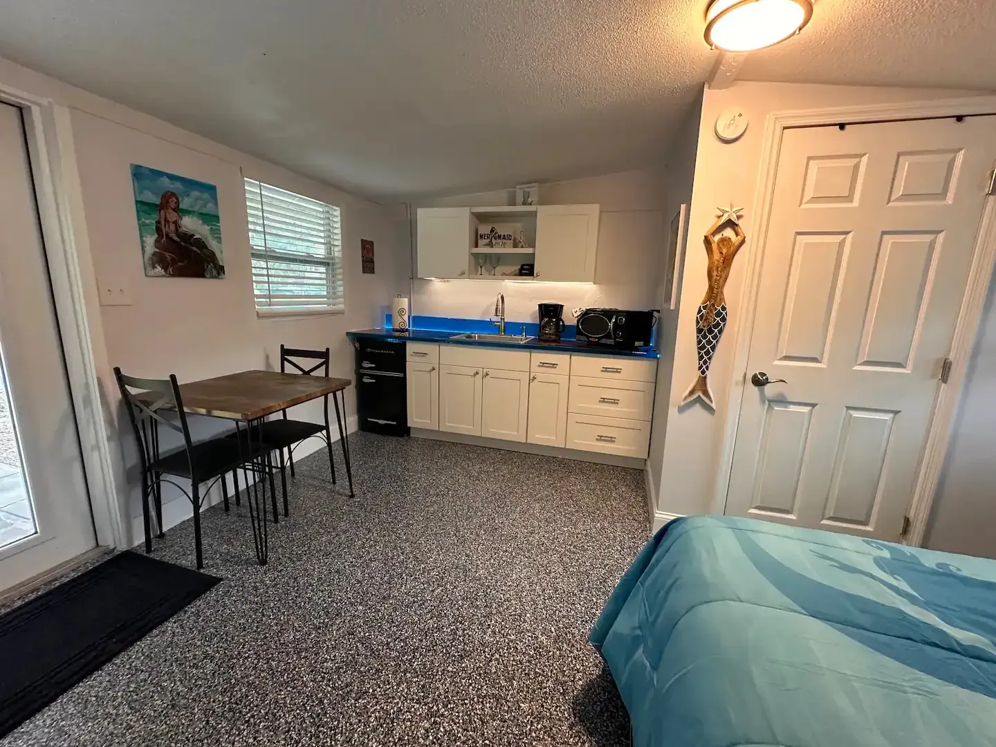 A bedroom with a bed , table , chairs and a kitchen.