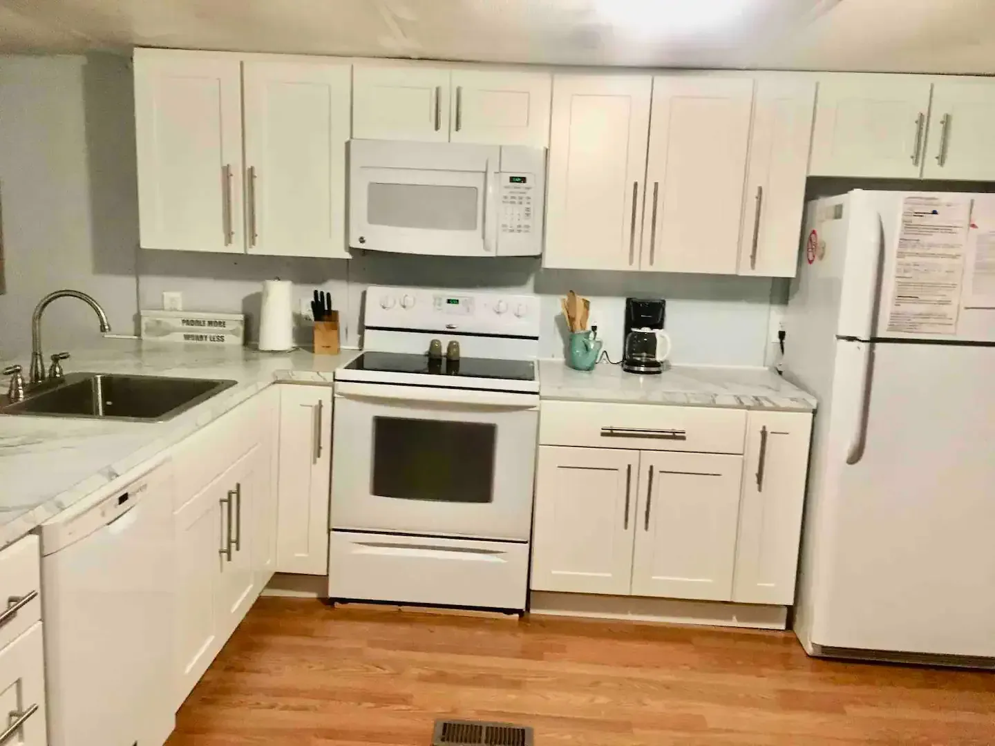 A kitchen with white cabinets , a stove , microwave , refrigerator and sink.
