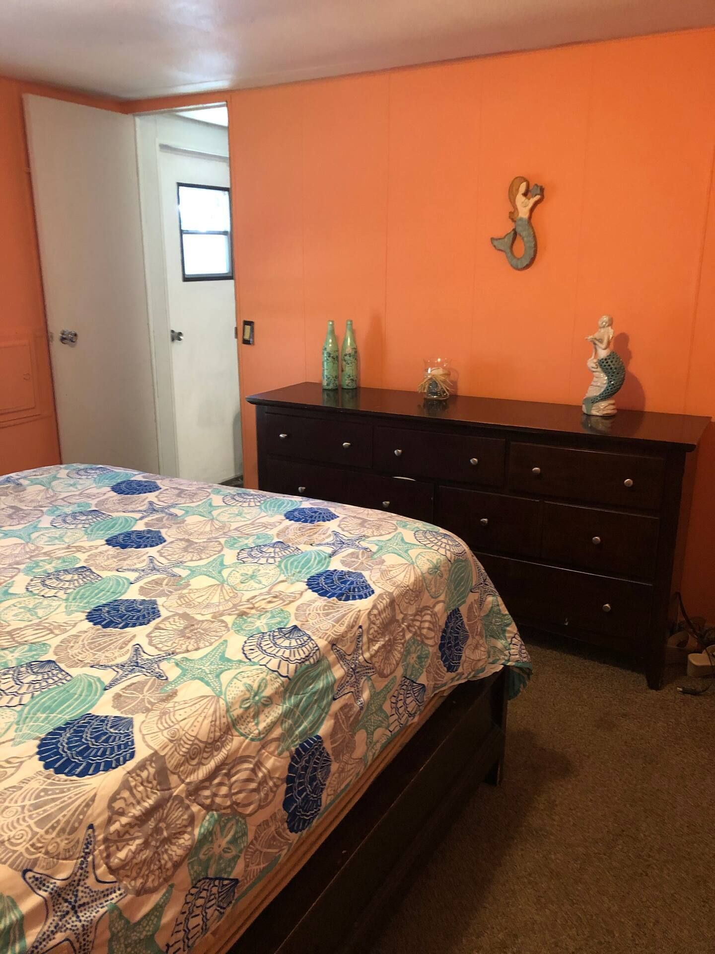A bedroom with a bed , dresser , and orange walls.