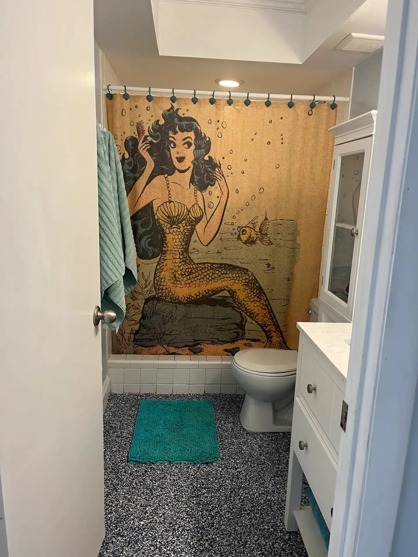 A bathroom with a shower curtain with a picture of a mermaid on it.