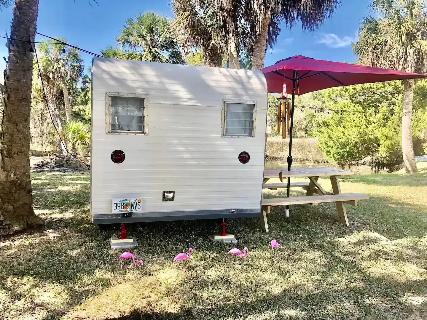 A white trailer with a red umbrella and a picnic table in a field.