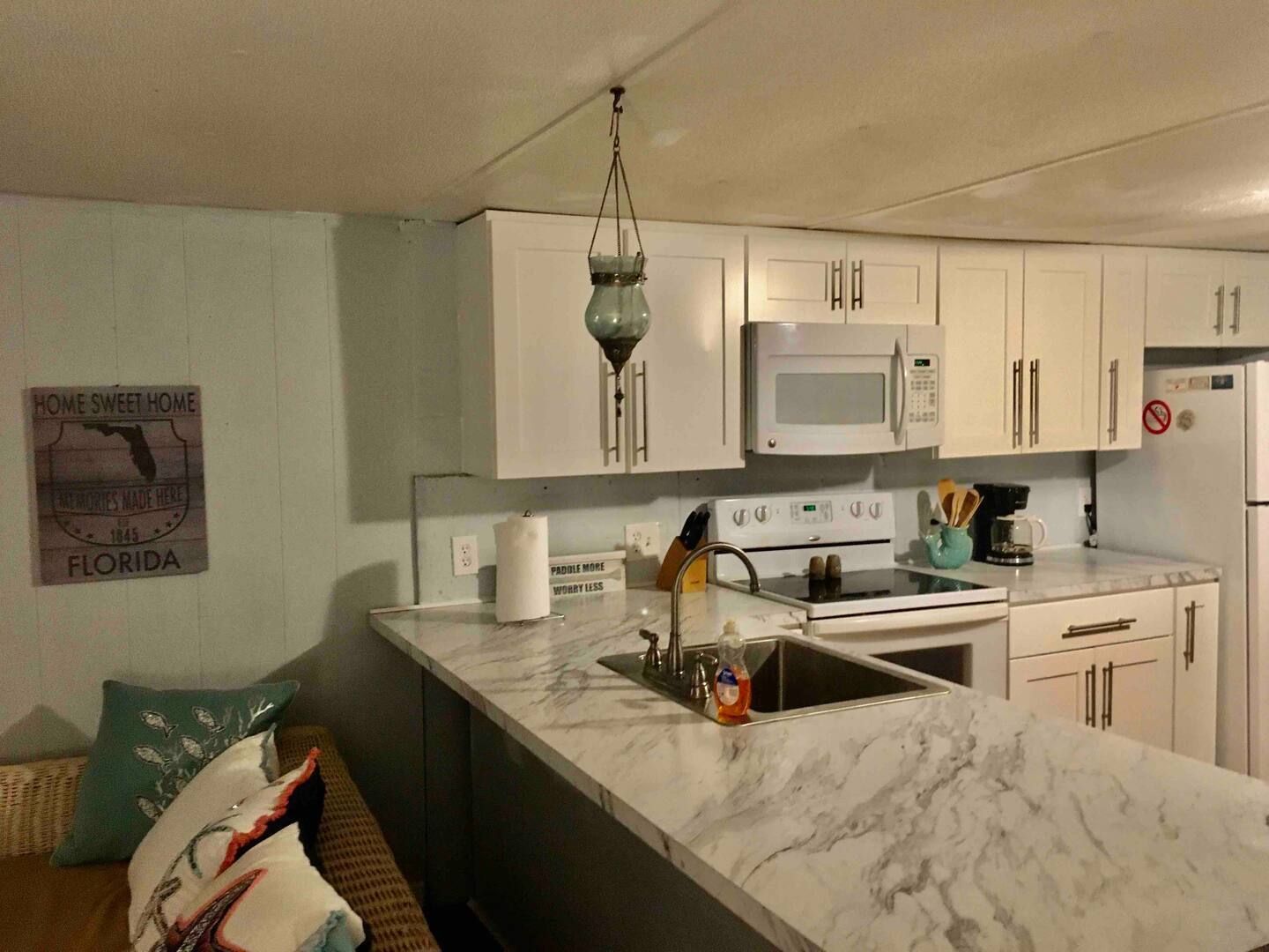 A kitchen with white cabinets , a sink , stove , microwave and refrigerator.