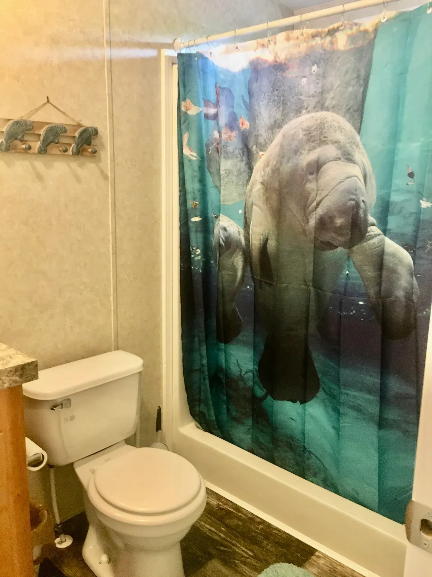 A bathroom with a toilet , shower , and shower curtain with a manatee on it.