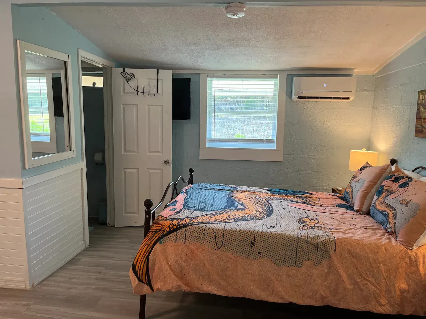 A bedroom with a bed , mirror , air conditioner and a window.
