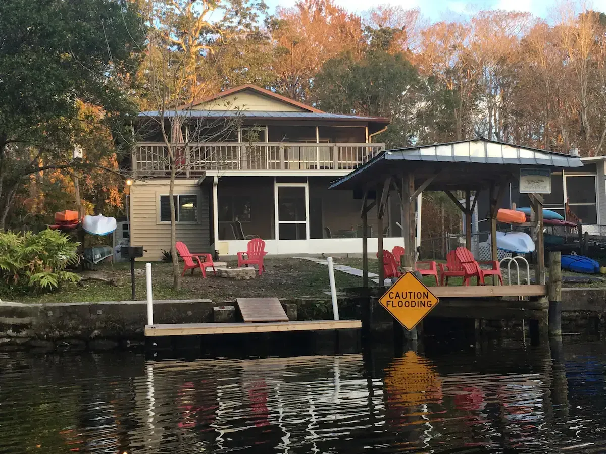 A house is sitting on top of a body of water next to a dock.