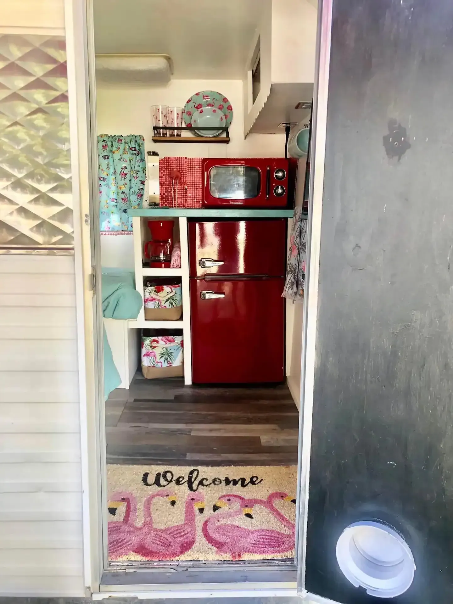 A kitchen with a red refrigerator , microwave , and welcome mat.
