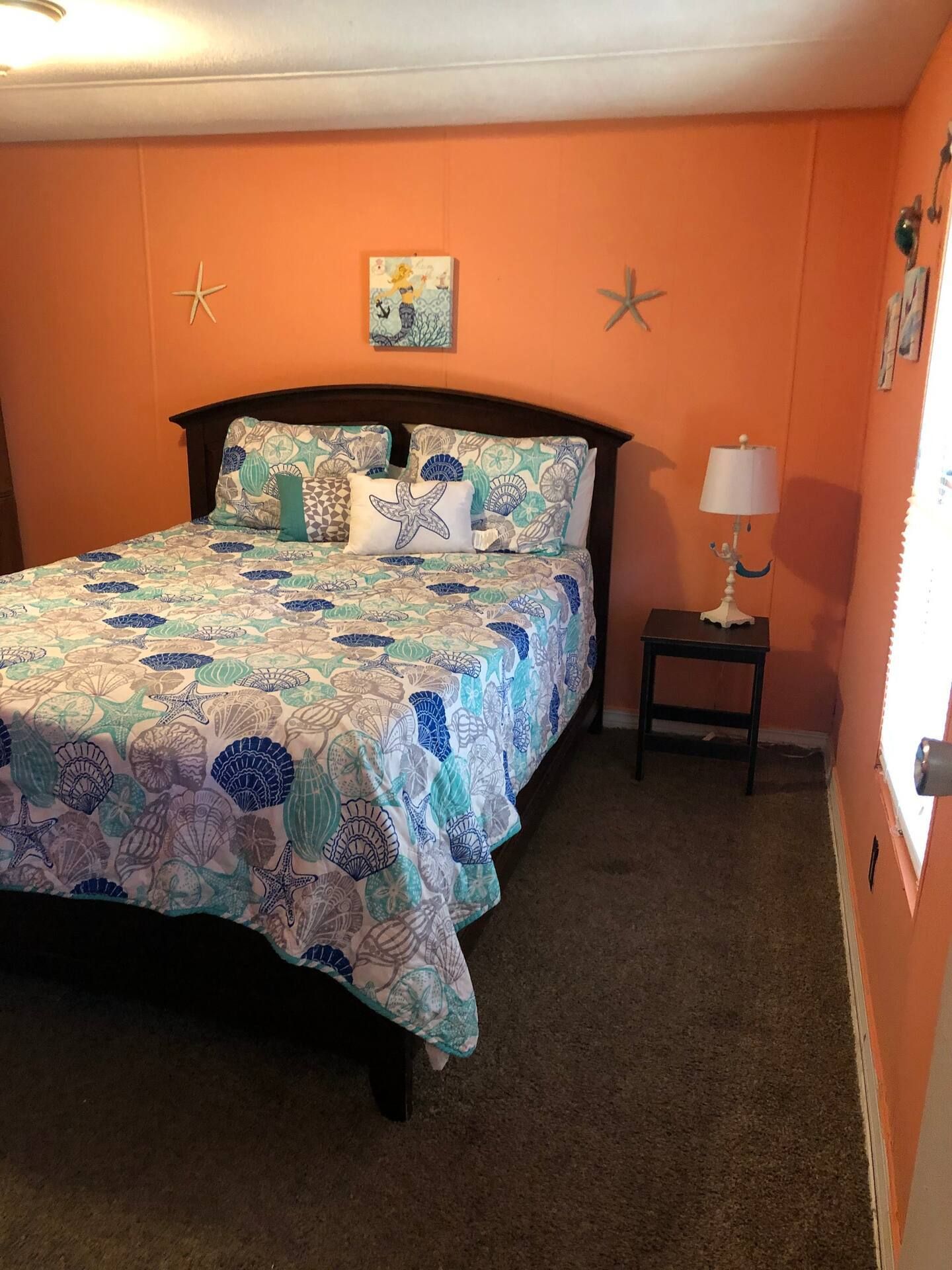 A bedroom with a bed , nightstand , lamp and starfish on the wall.