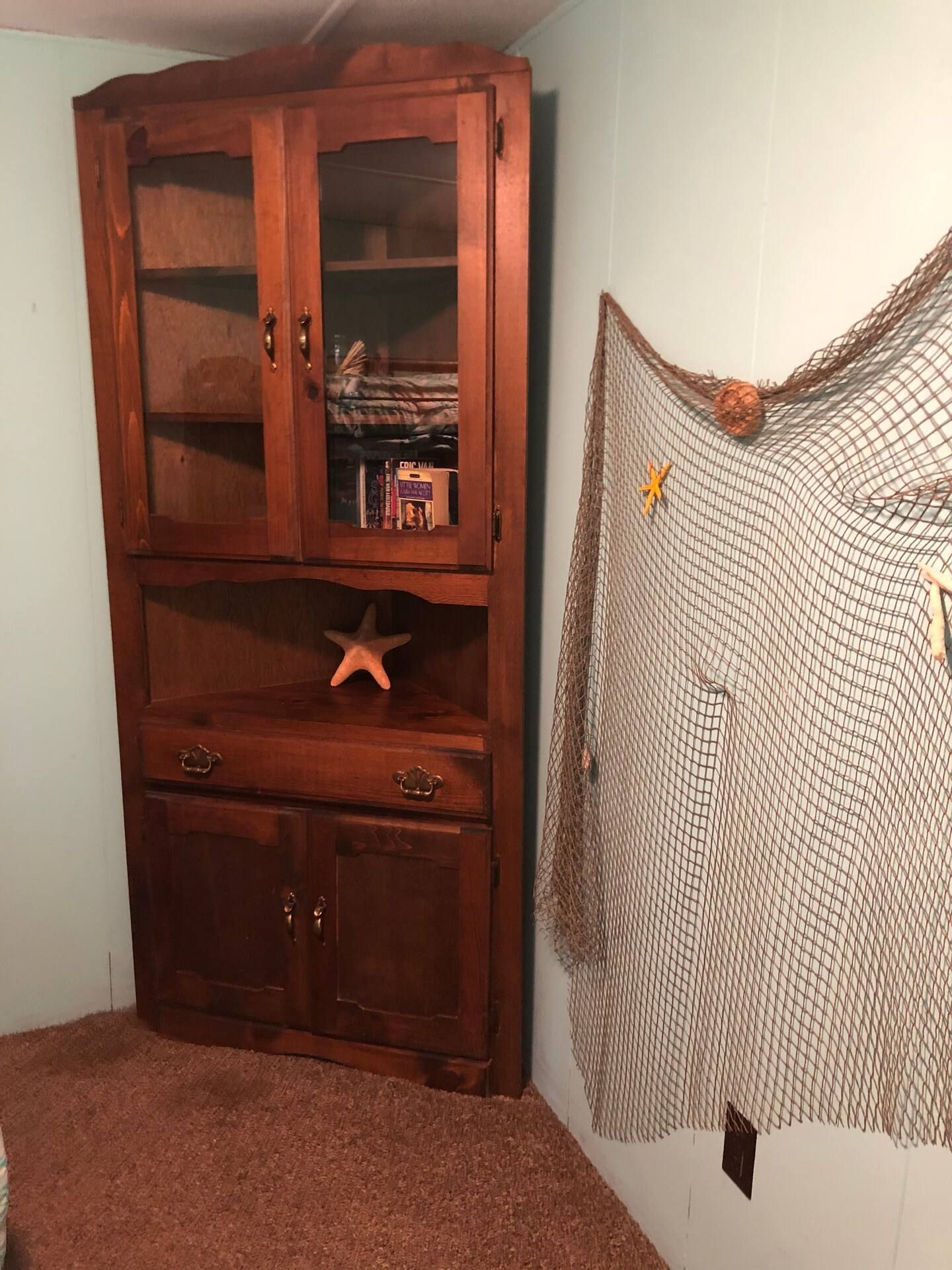 A room with a corner cabinet and a fishing net on the wall.