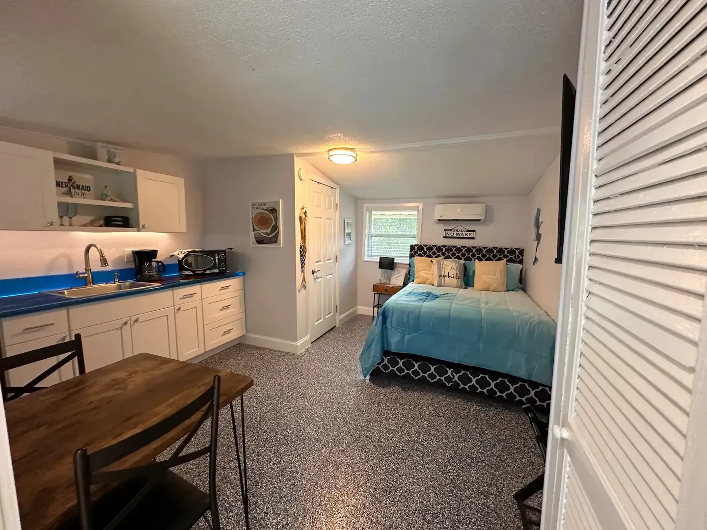 A bedroom with a bed , table , chairs and a kitchen.