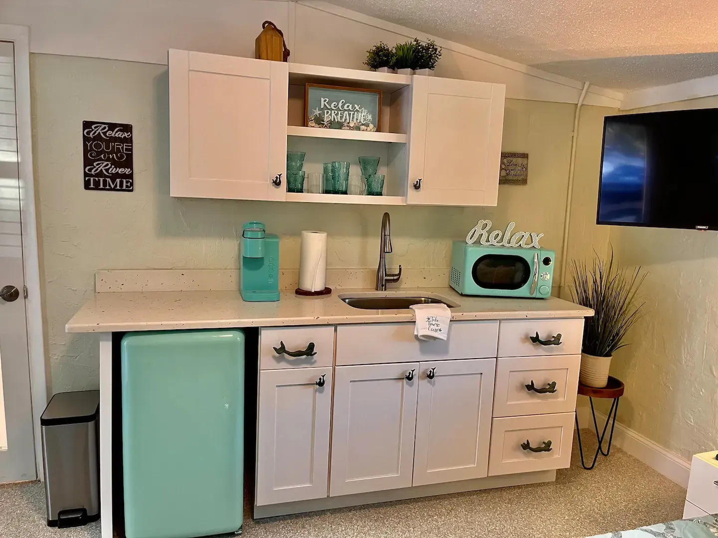 A kitchen with a sink , refrigerator , microwave and television.