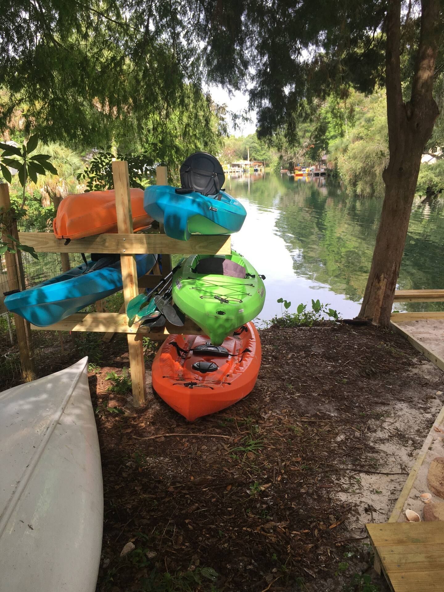A bunch of kayaks are stacked on top of each other next to a river.