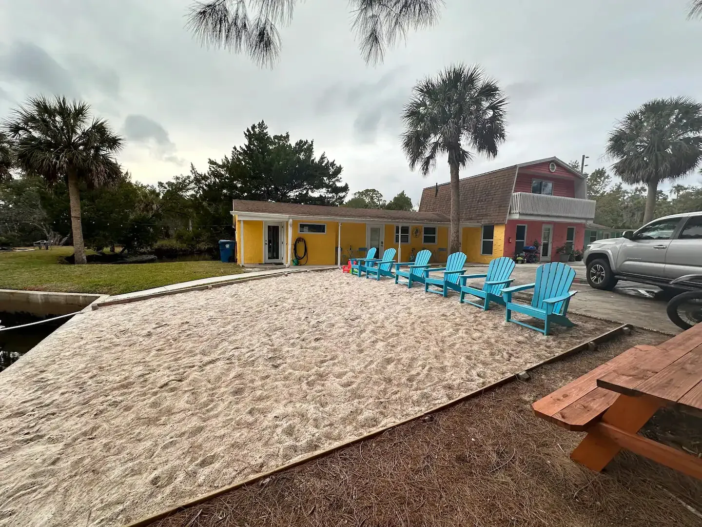 A row of blue chairs are lined up on a sandy beach in front of a house.