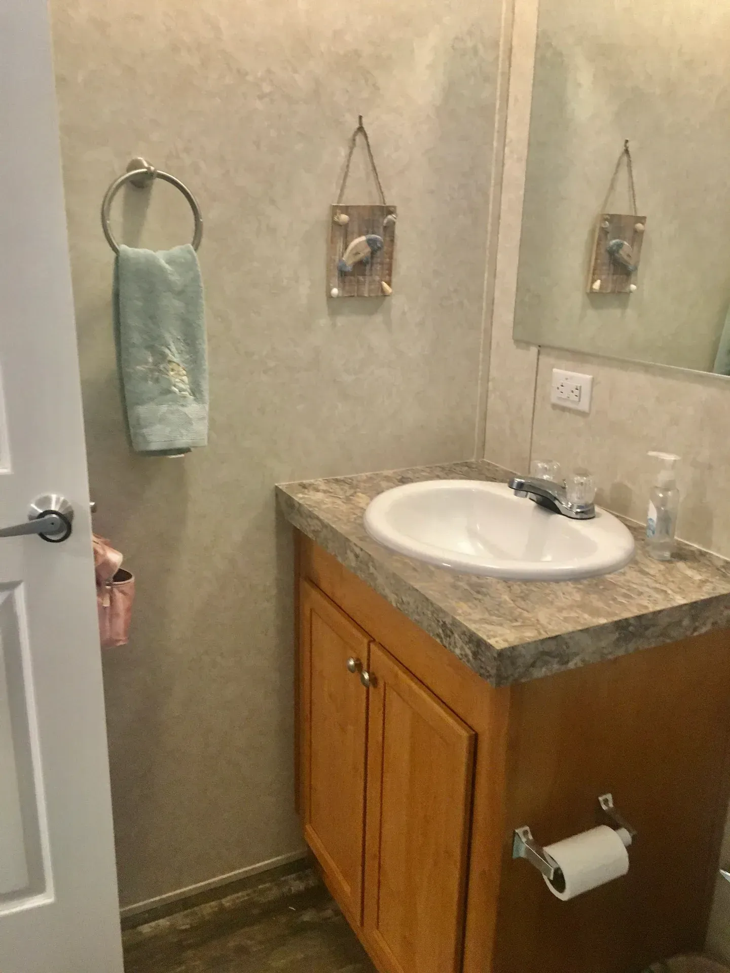 A bathroom with a sink , mirror and towel hanging on the wall.