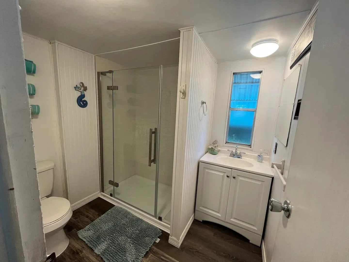 A bathroom with a toilet , sink , shower and window.