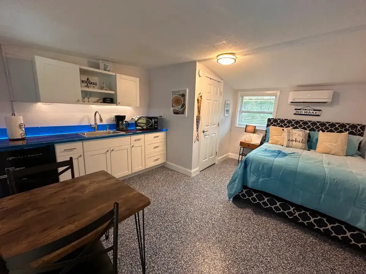 A bedroom with a bed , table , chairs and a kitchen.