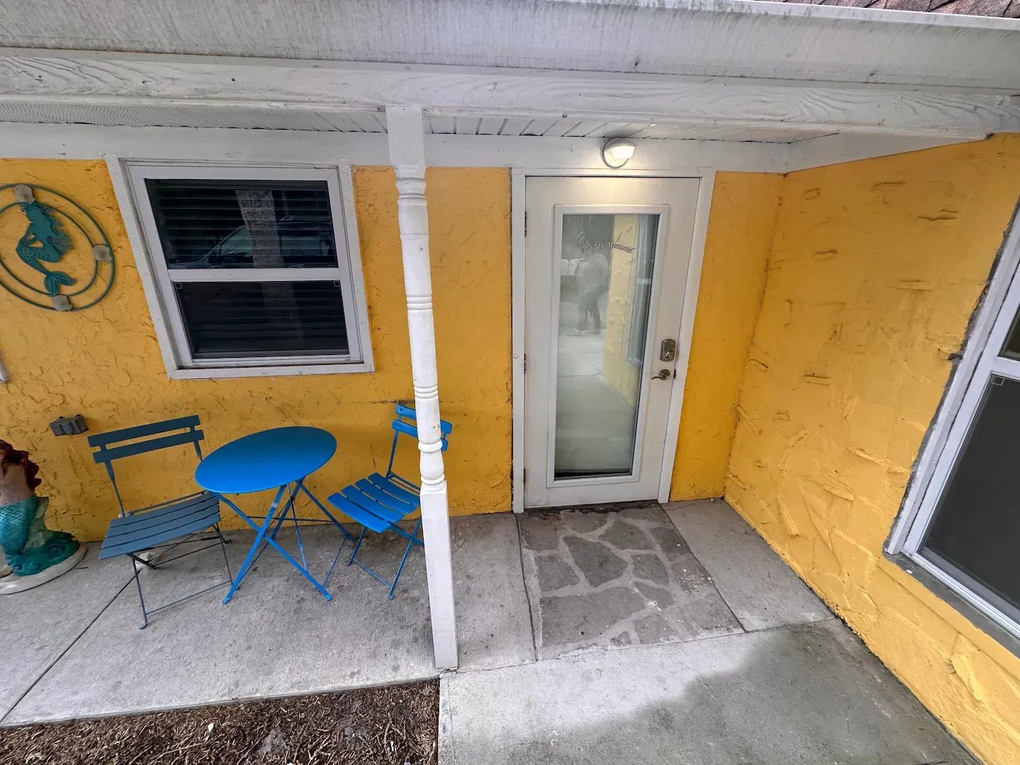 A yellow house with a blue table and chairs on the porch.