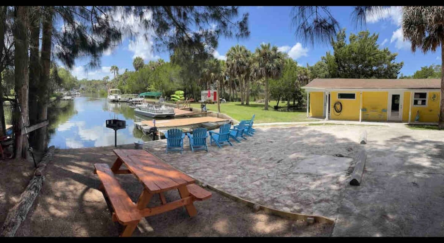 A picnic table and chairs are sitting in front of a house next to a body of water.