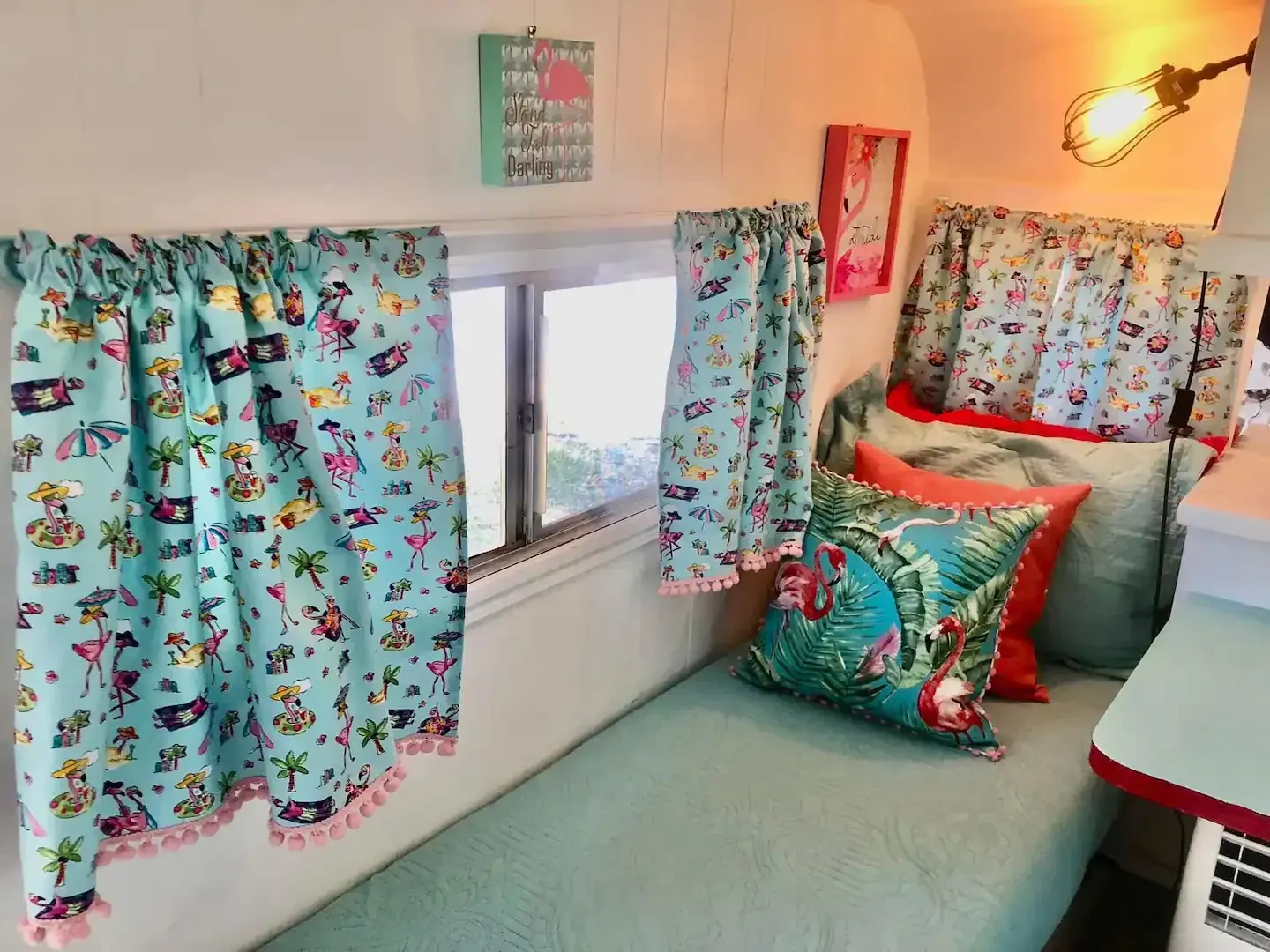 A camper with a bed , pillows , curtains and a window.
