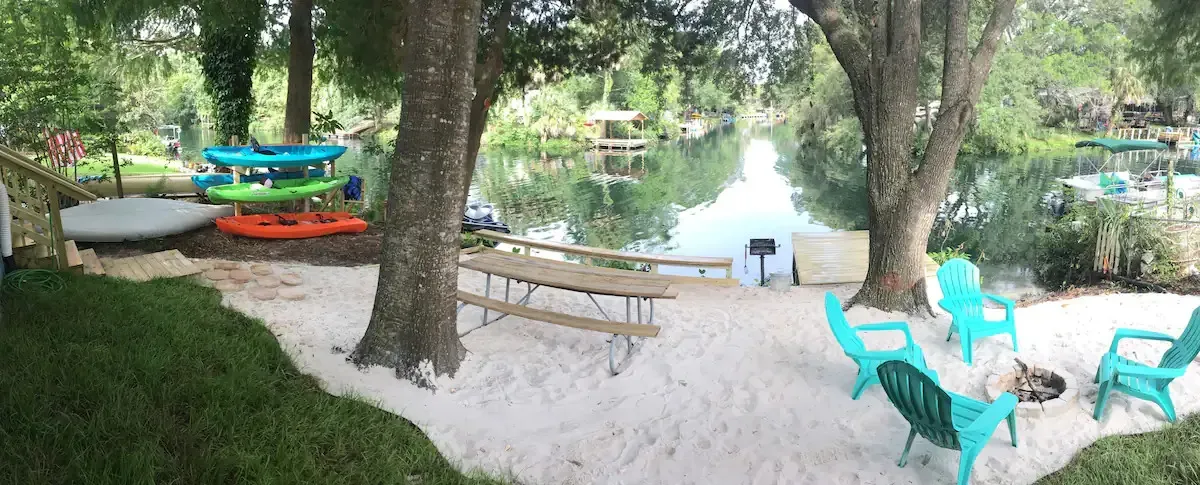 A picnic table and chairs are sitting in the sand near a body of water.