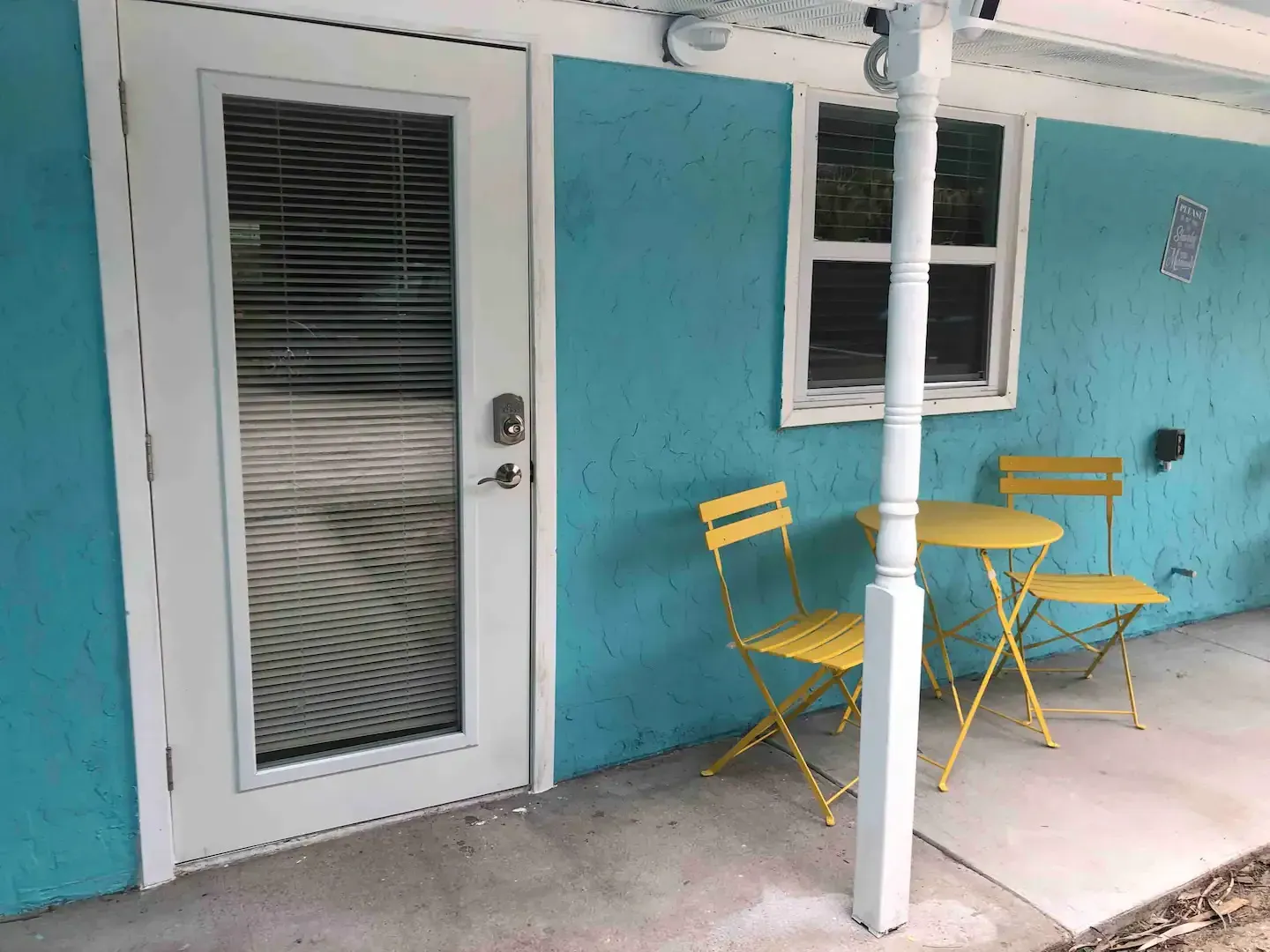 A blue house with yellow chairs and a table on the porch.
