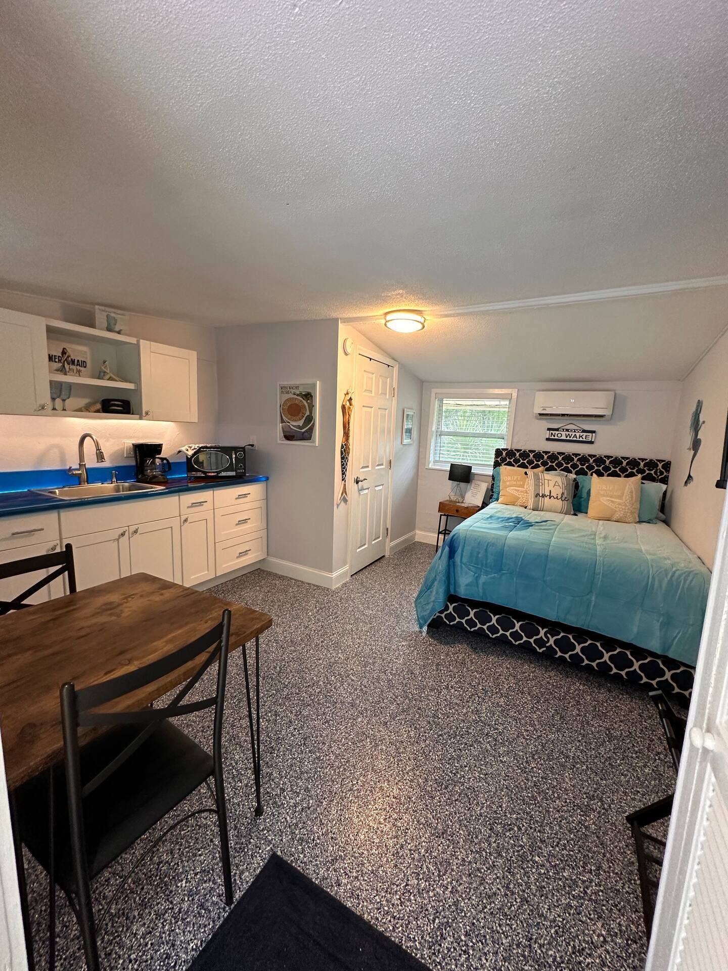 A bedroom with a bed , table , chairs and a kitchen.