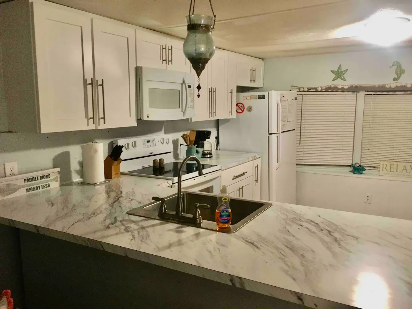 A kitchen with white cabinets , a sink , stove , microwave and refrigerator.
