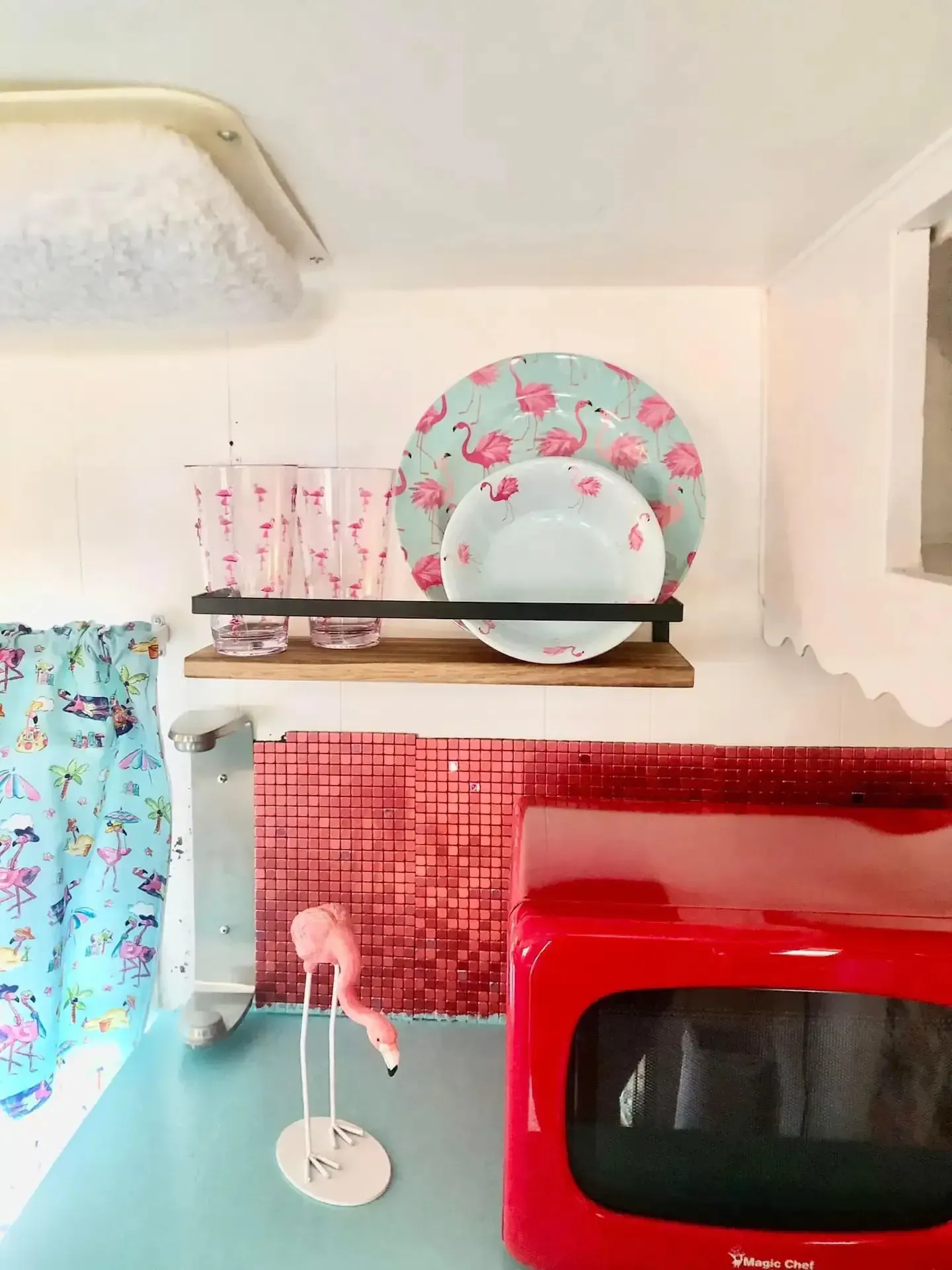 A red microwave and a shelf with plates and glasses on it