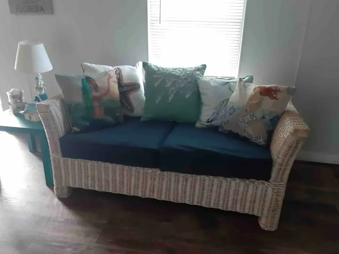 A white wicker couch with blue cushions and pillows in a living room.