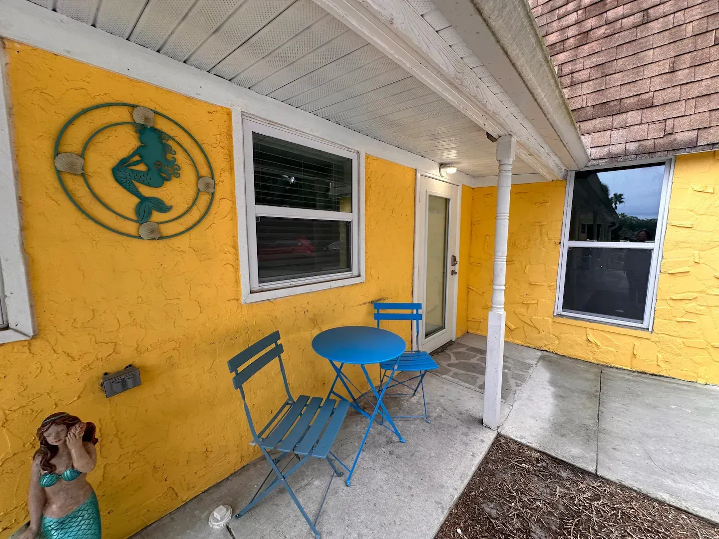 A yellow house with a table and chairs on the porch.