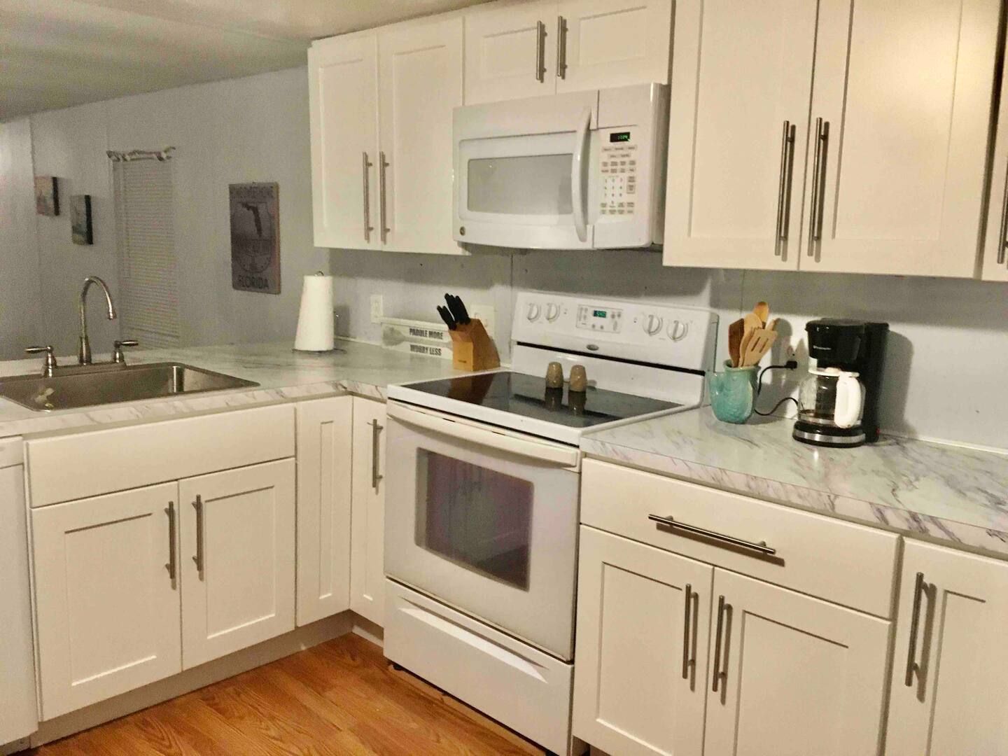 A kitchen with white cabinets , a stove , a microwave , and a sink.
