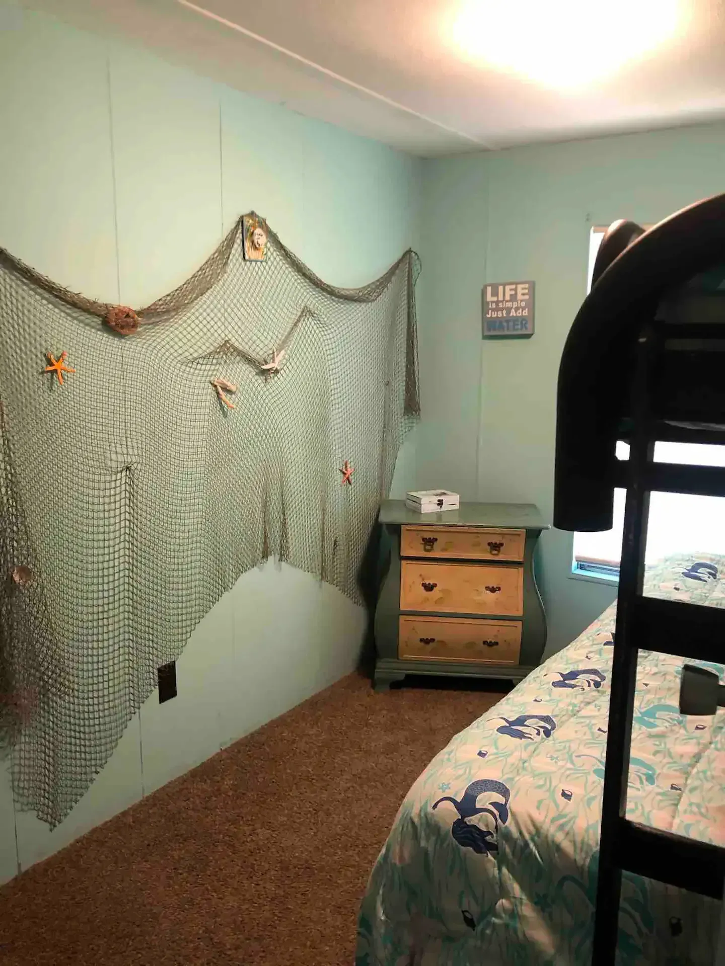 A bedroom with a bunk bed , dresser , and fishing net on the wall.