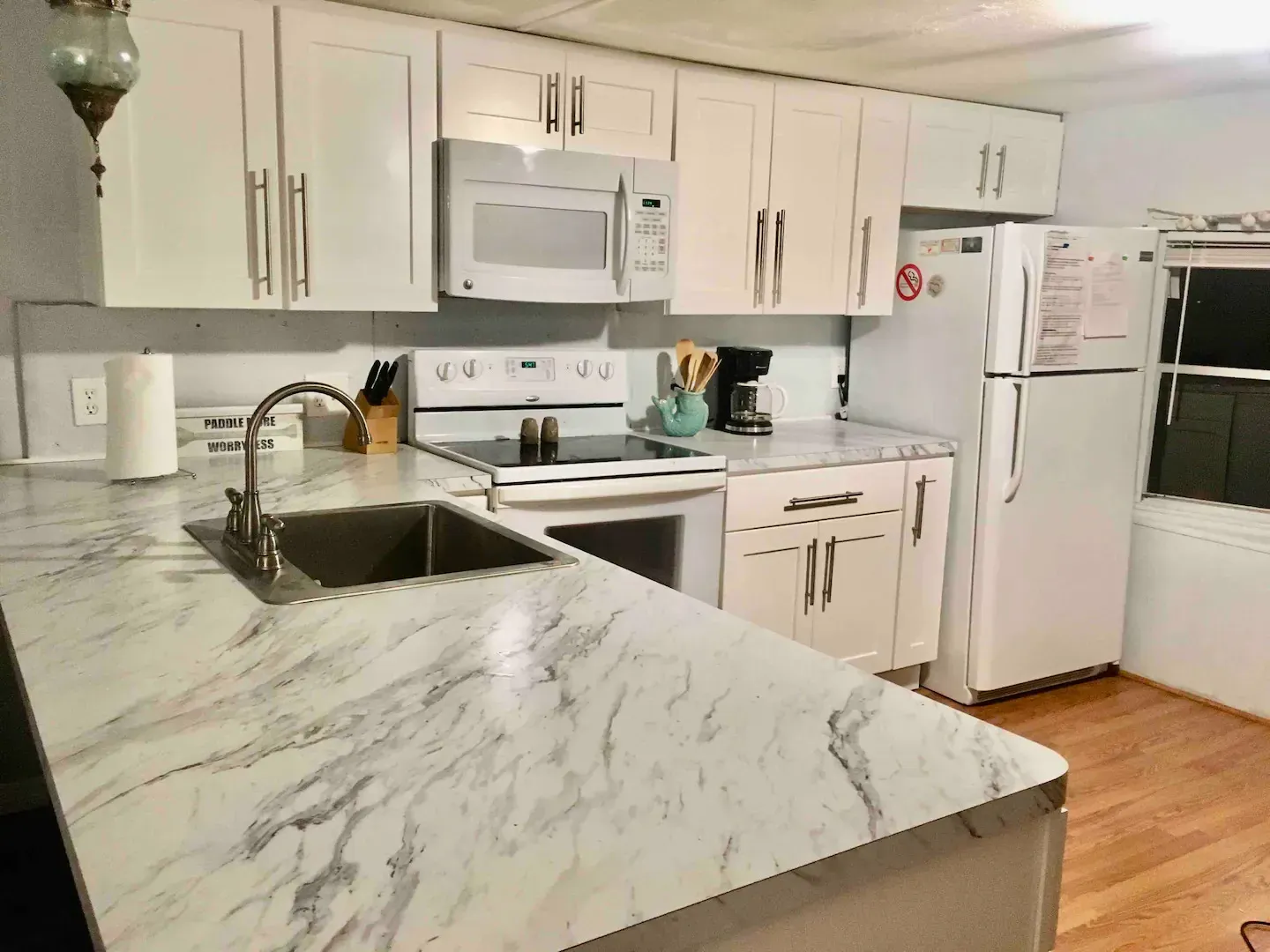 A kitchen with white cabinets , marble counter tops , a sink , stove and refrigerator.