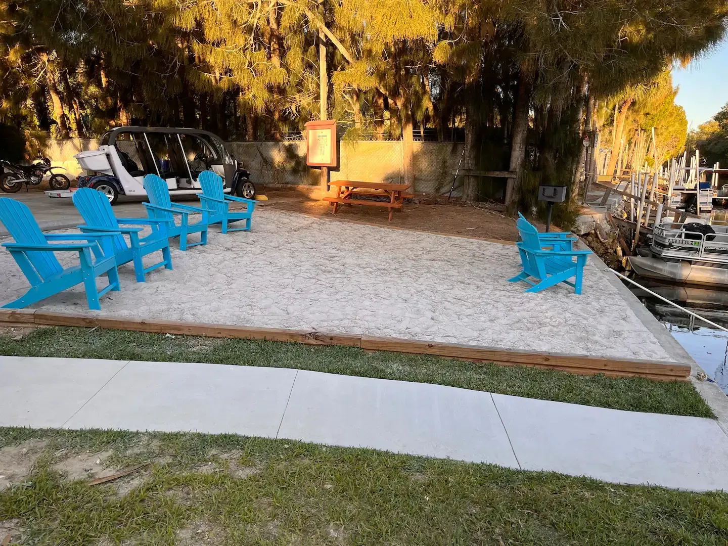 A row of blue chairs sitting on top of a sandy area next to a river.
