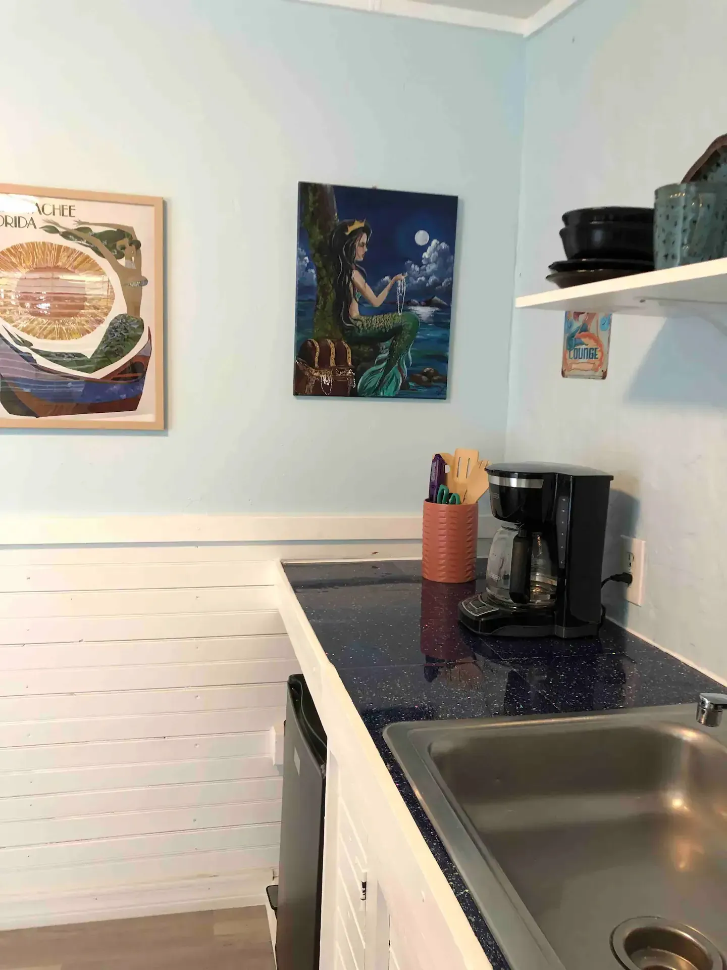 A kitchen with a sink , coffee maker , and a painting on the wall.