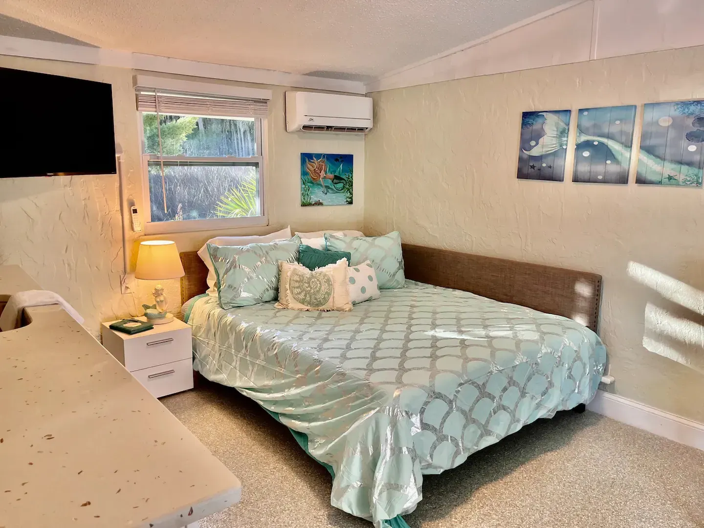 A bedroom with a bed , nightstand , television and paintings on the wall.