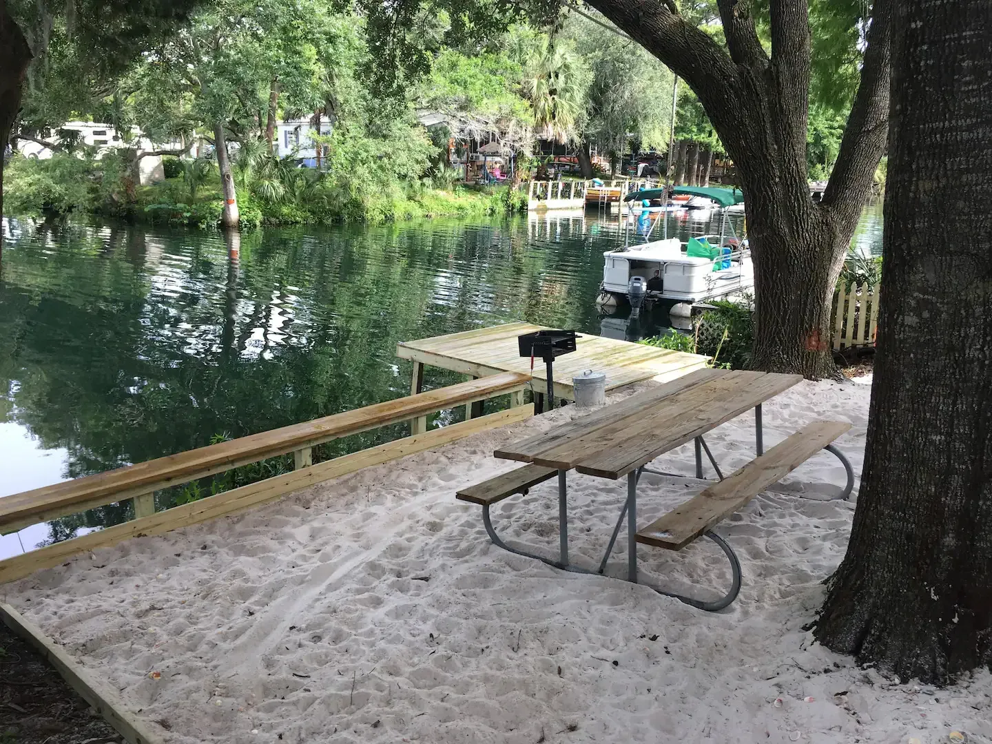 A picnic table is sitting in the sand near a lake.