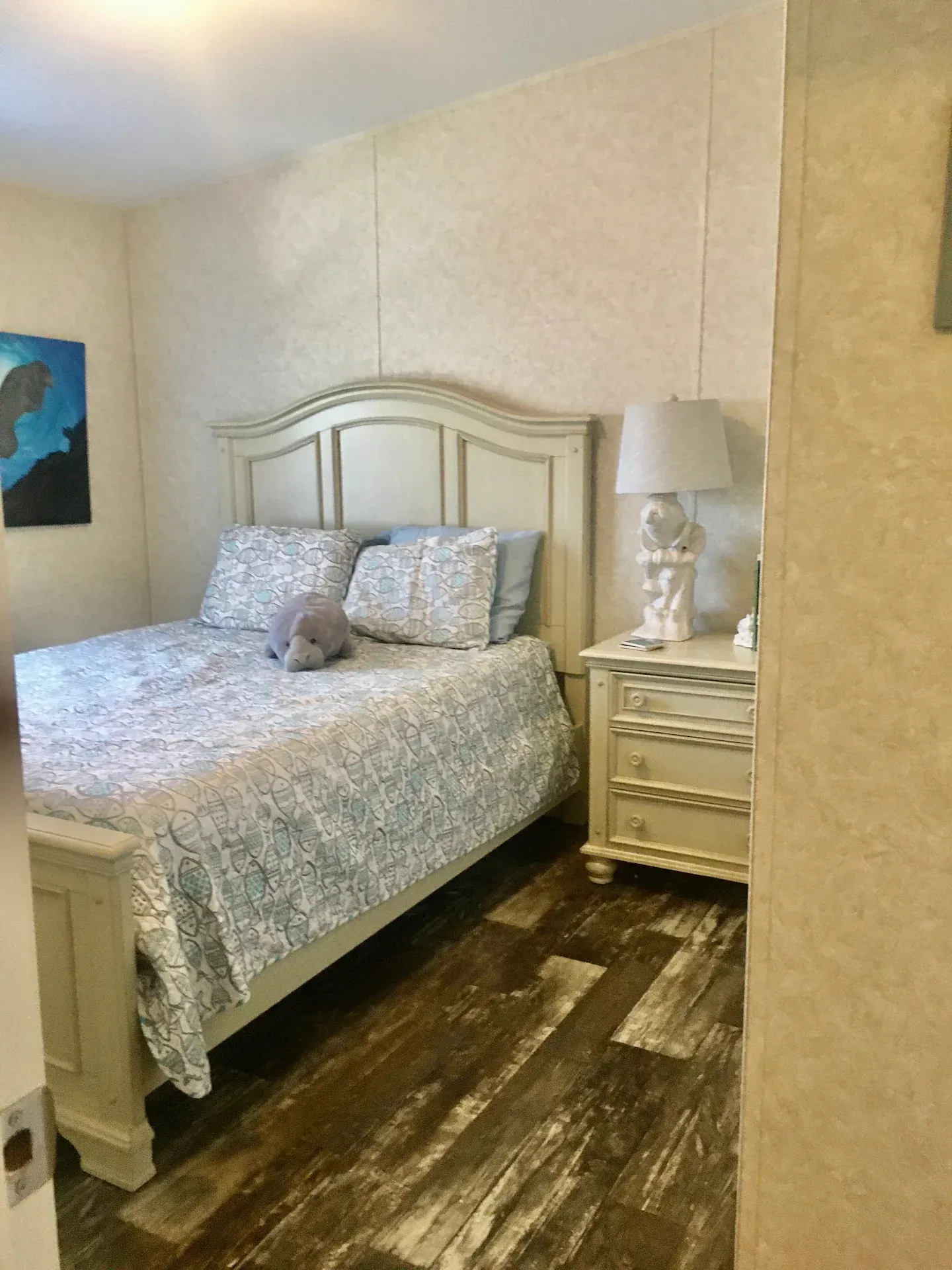 A bedroom with a bed , nightstand , lamp and painting on the wall.