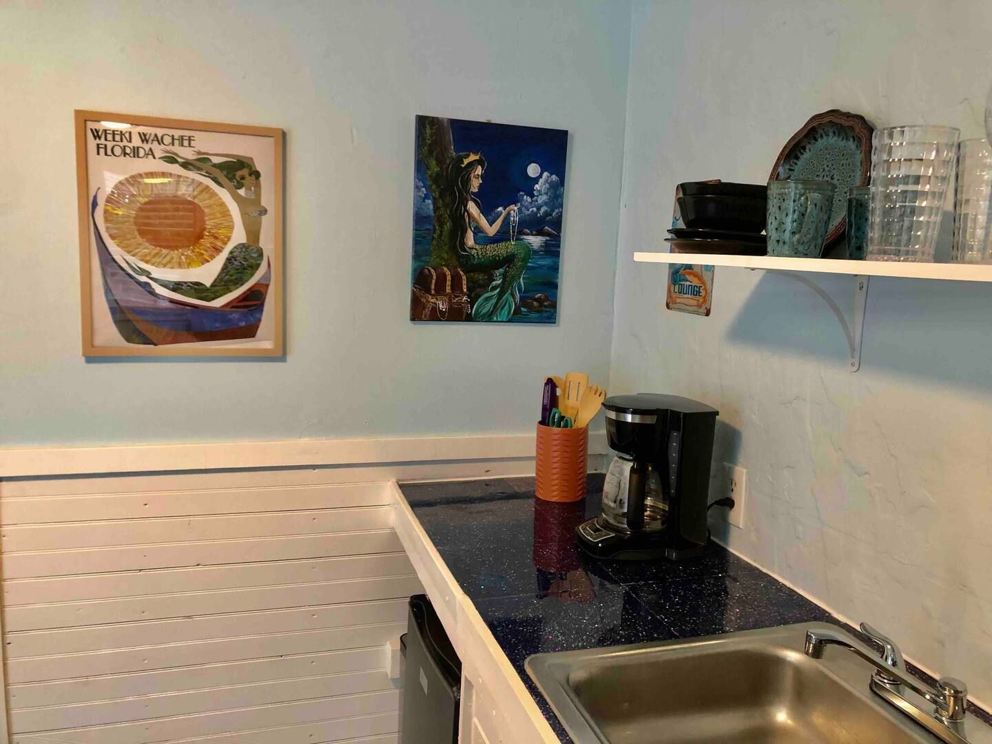A kitchen with a sink , coffee maker , and a painting on the wall.