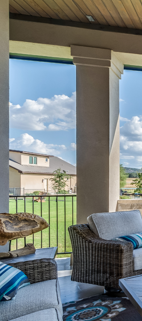 Patio with wicker furniture, overlooking a grassy yard and houses under a blue sky.