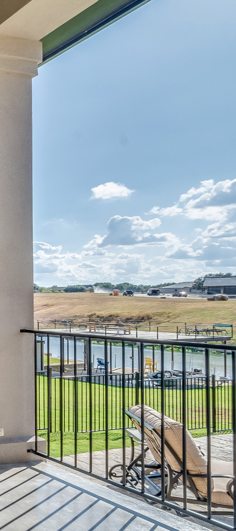 Balcony view with railing overlooking a field, water, and cloudy sky.